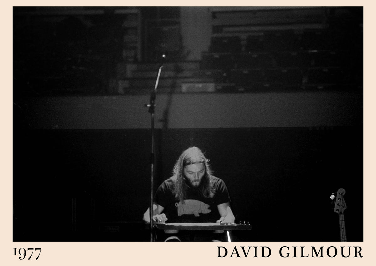 Black and white photo of David Gilmour playing lap steel guitar on stage, with 1977 and David Gilmour on a cream border