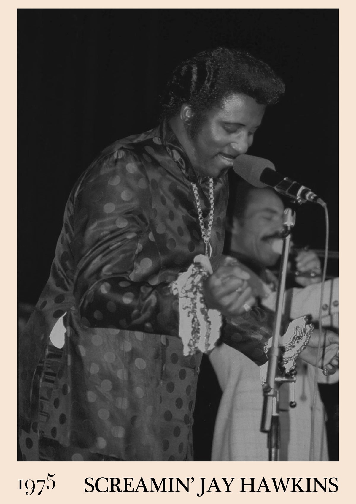 Black and white photo of Screamin' Jay Hawkins singing into a microphone on stage in a polka-dot jacket, 1975