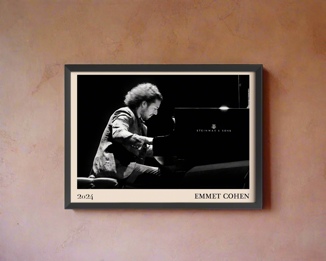 2024 photo of Emmet Cohen crafted into a black framed-poster, hanging on a peach coloured concrete wall in dappled sunlight