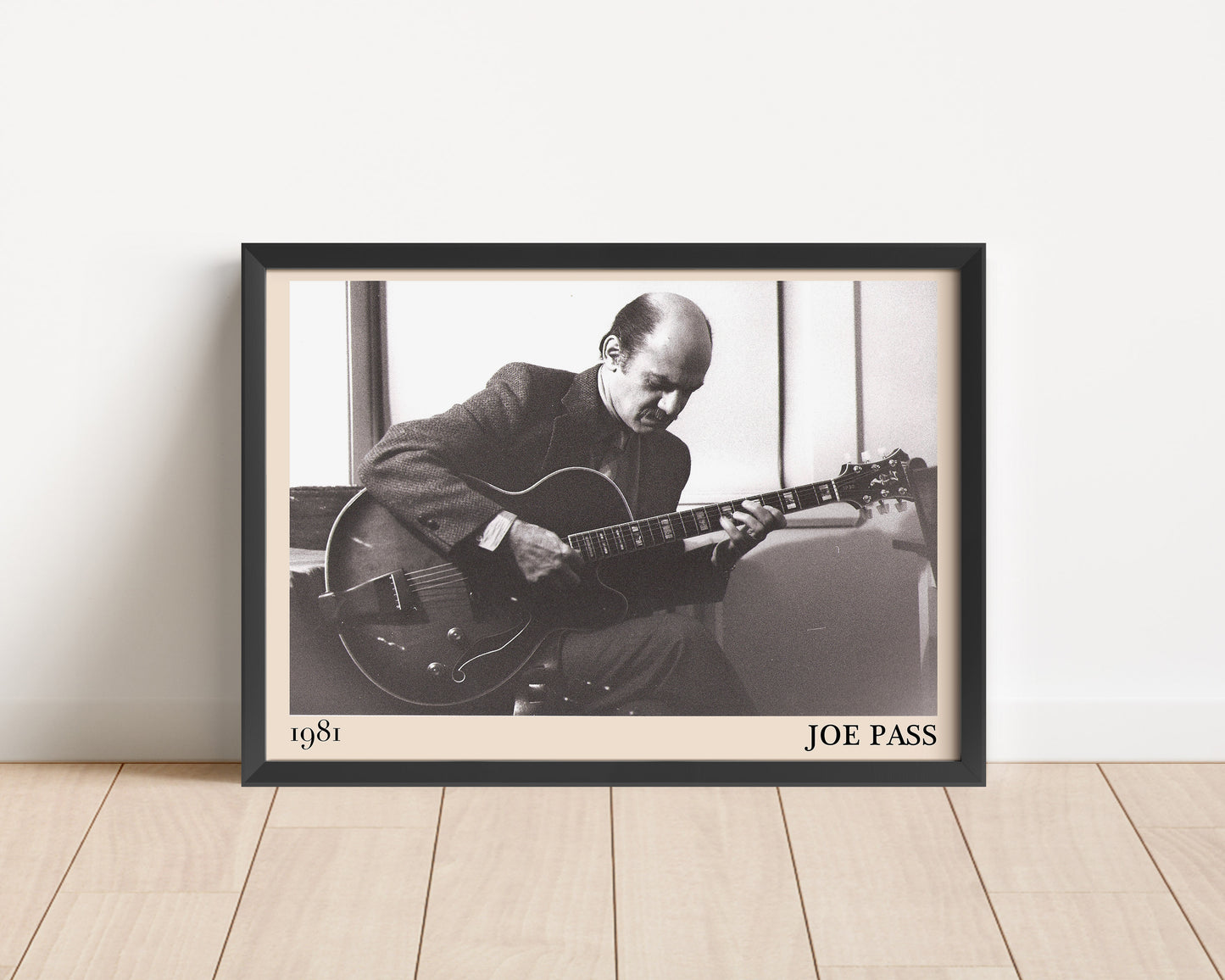 1981 photo of Joe Pass crafted into an elegant black-framed print. Leaning against a white wall