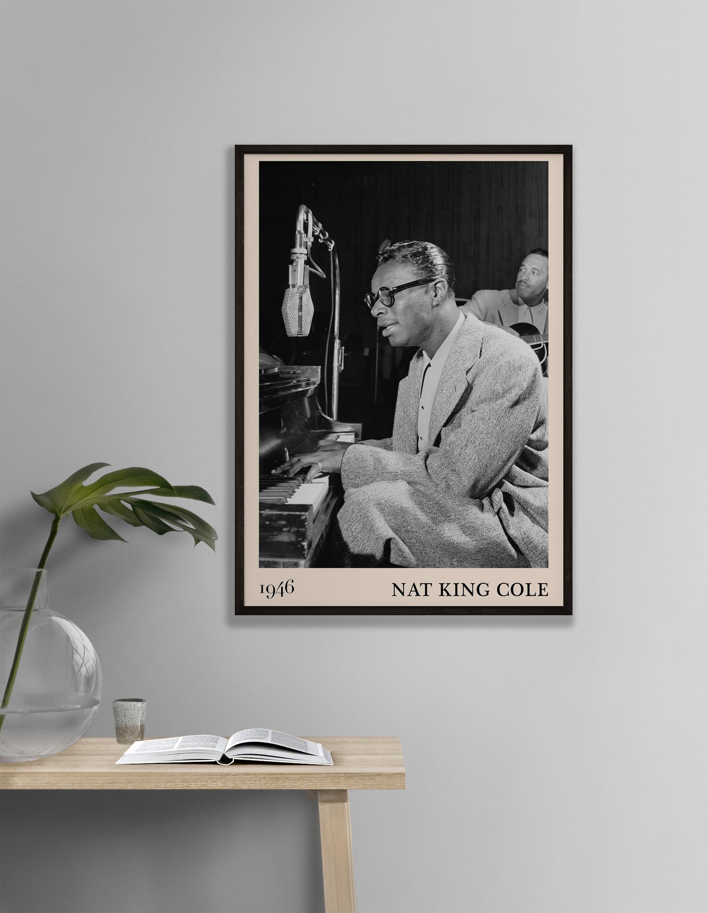 1946 picture of Nat King Cole playing a piano and singing. Picture crafted into a retro black framed jazz poster, with an off-white border. Poster is hanging on a grey living room wall