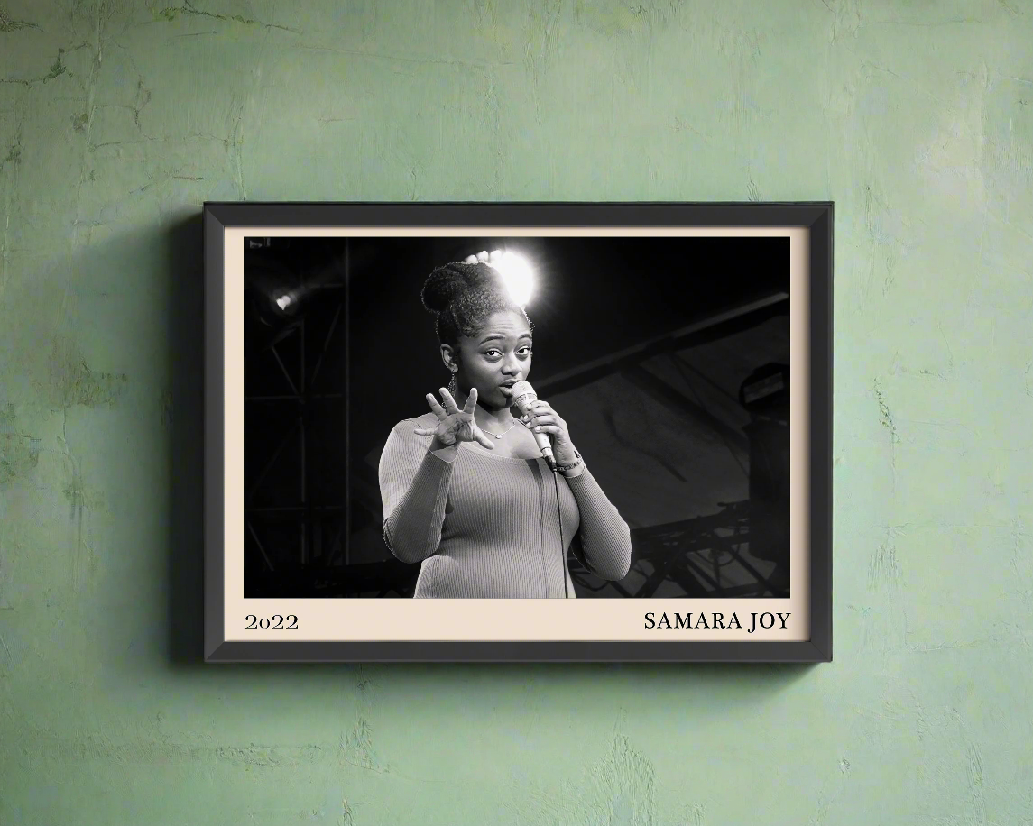 2022 photo of Samara Joy crafted into a black framed-poster, hanging on a light green concrete wall in dappled sunlight