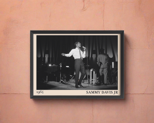 1964 picture of Sammy Davis Jr. Picture crafted into a black framed poster, with an off-white border. Poster is hanging on a peach wall