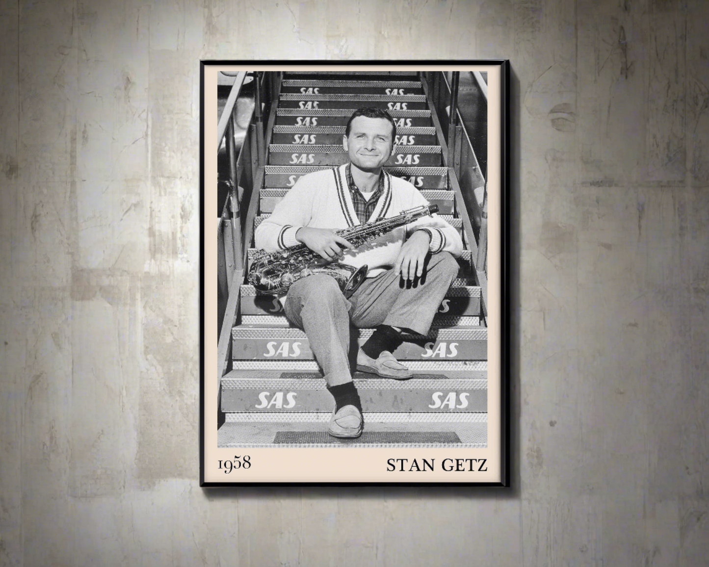 1958 picture of Stan Getz holding his saxophone. Picture crafted into a black framed poster, with an off-white border. Poster is hanging on a concrete wall