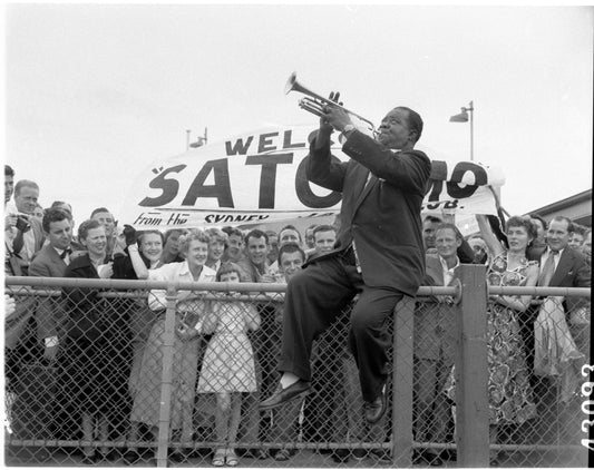 Louis Armstrong sitting on a fence in front of a crowd