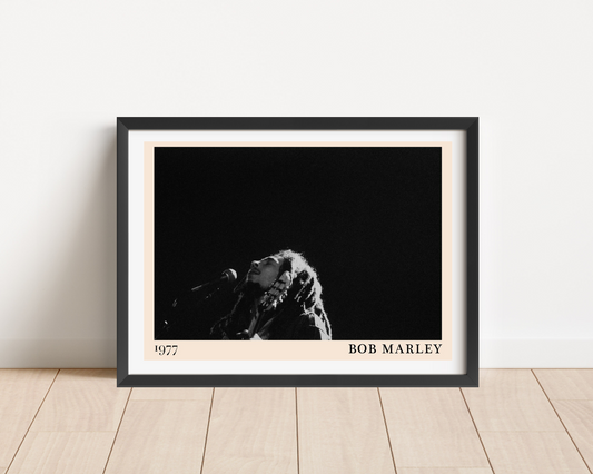 Bob Marley concert poster in a black frame, landscape mount on wood floor, features 1977 date and monochrome stage photo.