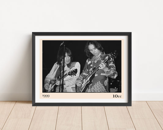 Framed print of 10cc on a wooden floor against a white wall, featuring a black and white concert photo of two guitarists on