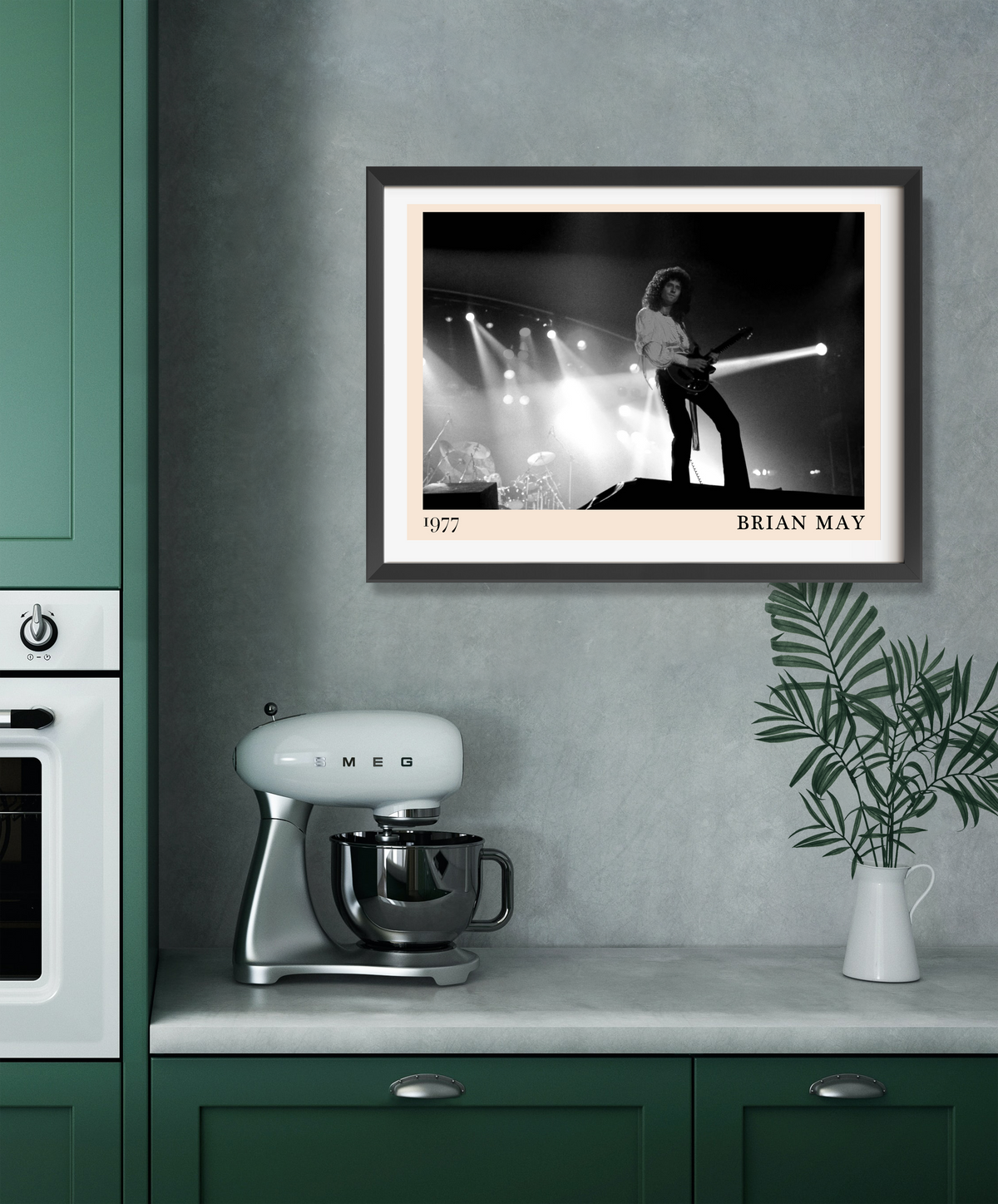 Framed print of Brian May performing on stage in 1977, displayed in a dark frame above a green kitchen counter with a Smeg