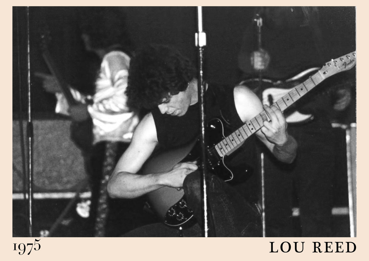 Black and white photo of Lou Reed bent over a Fender guitar on stage in 1975, with his name and the year printed below