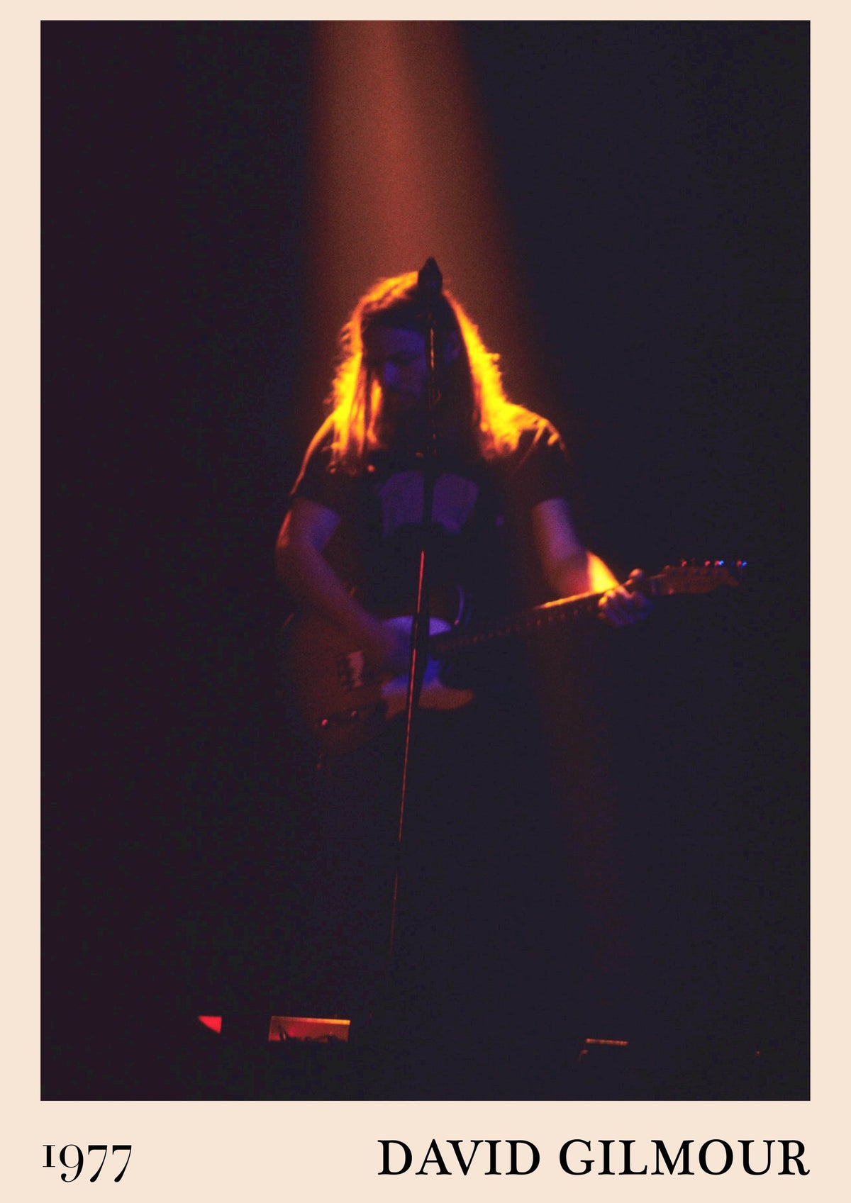 David Gilmour playing electric guitar at a microphone, lit from above by an amber spotlight, with 1977 and his name below