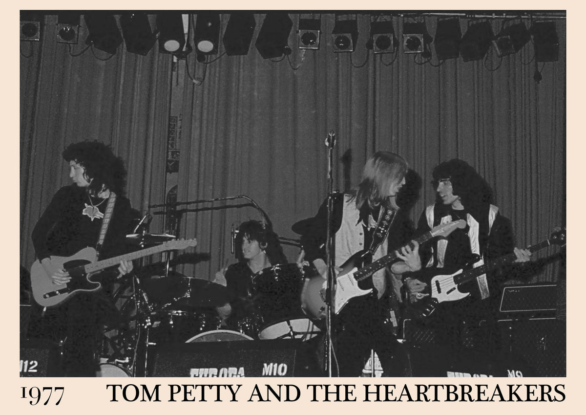 Black and white photo of Tom Petty and the Heartbreakers with Ron Blair on stage, 1977, band name printed below