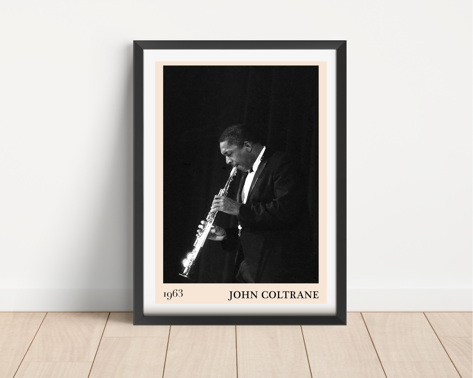 John Coltrane jazz poster mockup in a modern black frame on a wood floor, featuring a black and white saxophone portrait.