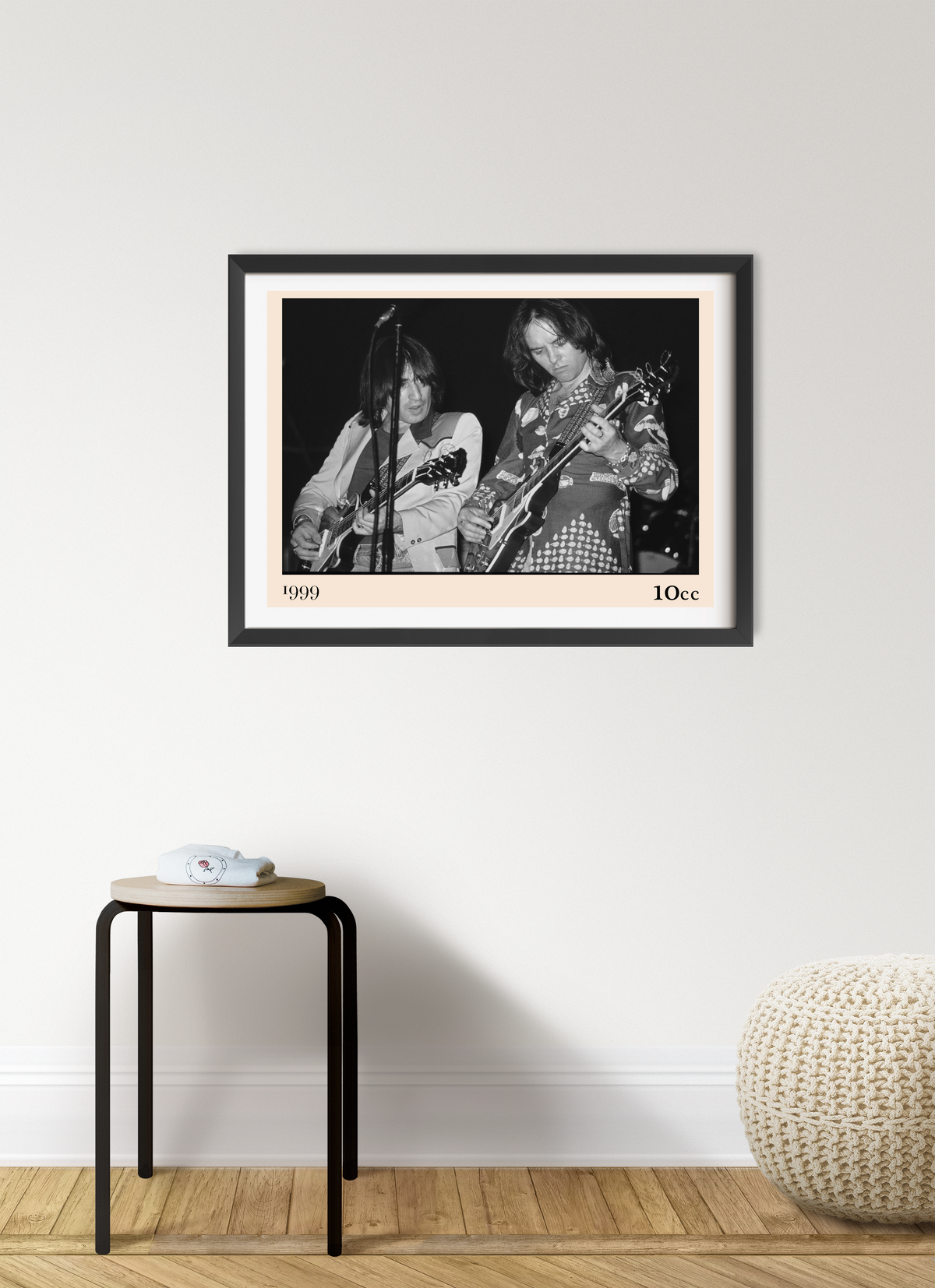 Framed 10cc rock concert print in black and white, dated 1999, showing two guitarists on stage, hung above a small wooden