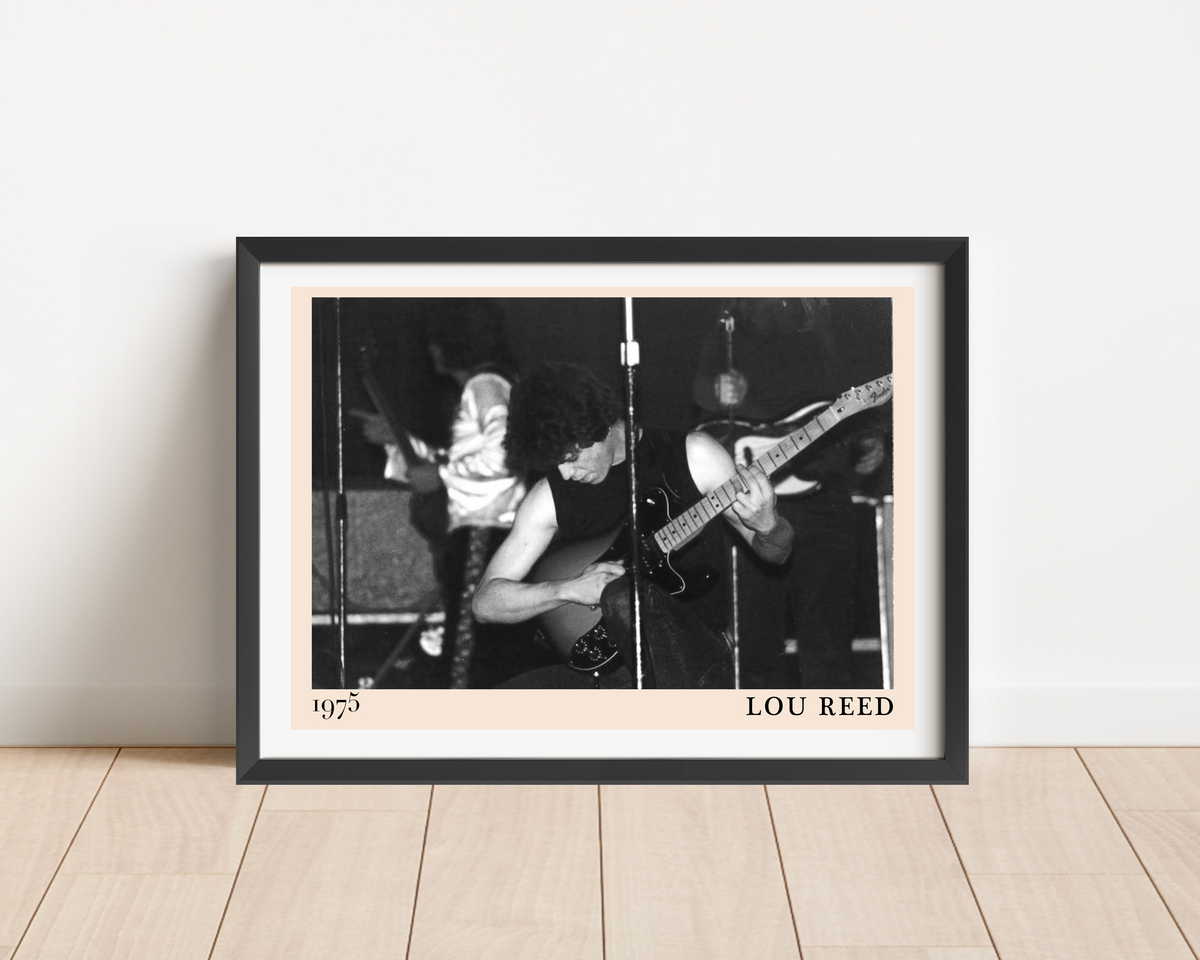 Black framed print of Lou Reed performing live in 1975, black and white concert photography, leaning against a white wall on