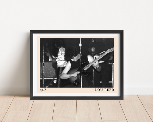 Black framed print of Lou Reed performing live in 1975, black and white concert photography, leaning against a white wall on