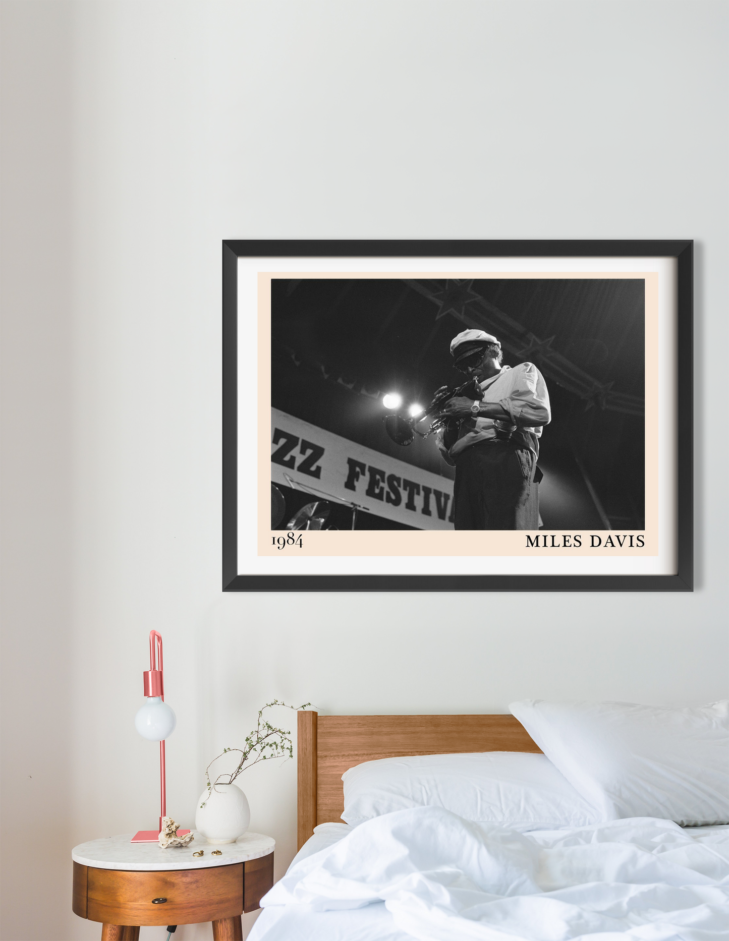 Miles Davis vintage jazz poster in a black frame, landscape 16 mount, displayed above a modern bed in a minimalist bedroom.