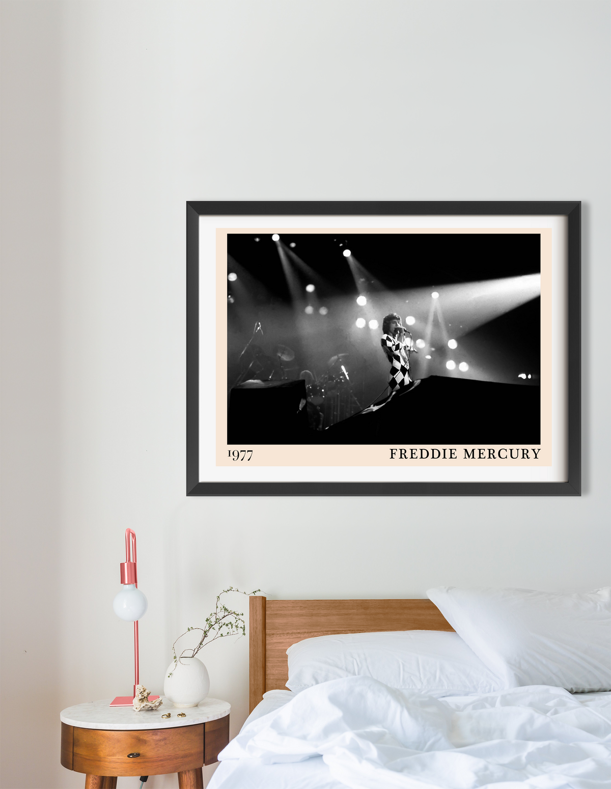Freddie Mercury 1977 framed print in black frame with cream mount, hung above a wooden bed in a minimal bedroom setting.