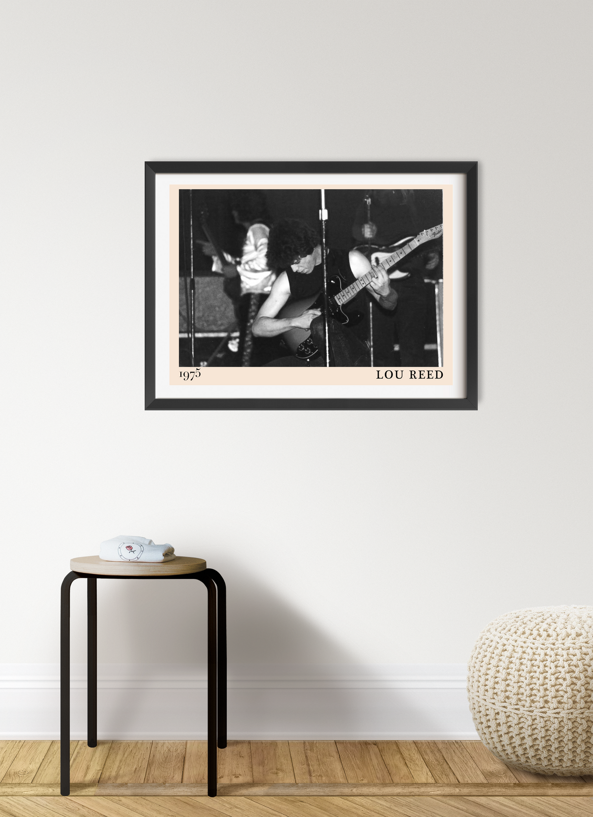 Lou Reed 1975 framed print in black frame with peach mount, featuring a black and white concert photo, hung above a wooden