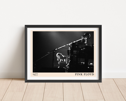 Pink Floyd rock concert poster mockup in landscape frame on wood floor, features black and white 1977 live stage photo.
