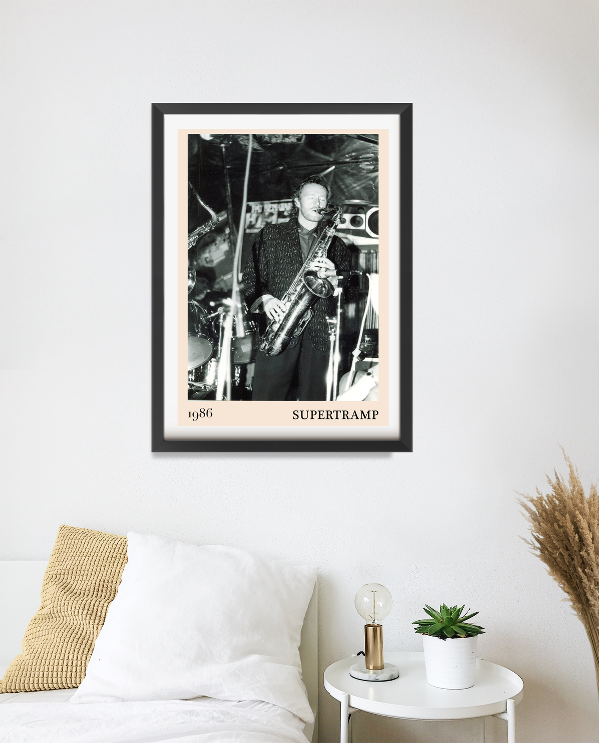 Framed Supertramp 1986 concert print on a white bedroom wall, featuring a black-and-white photo of a saxophonist on stage.