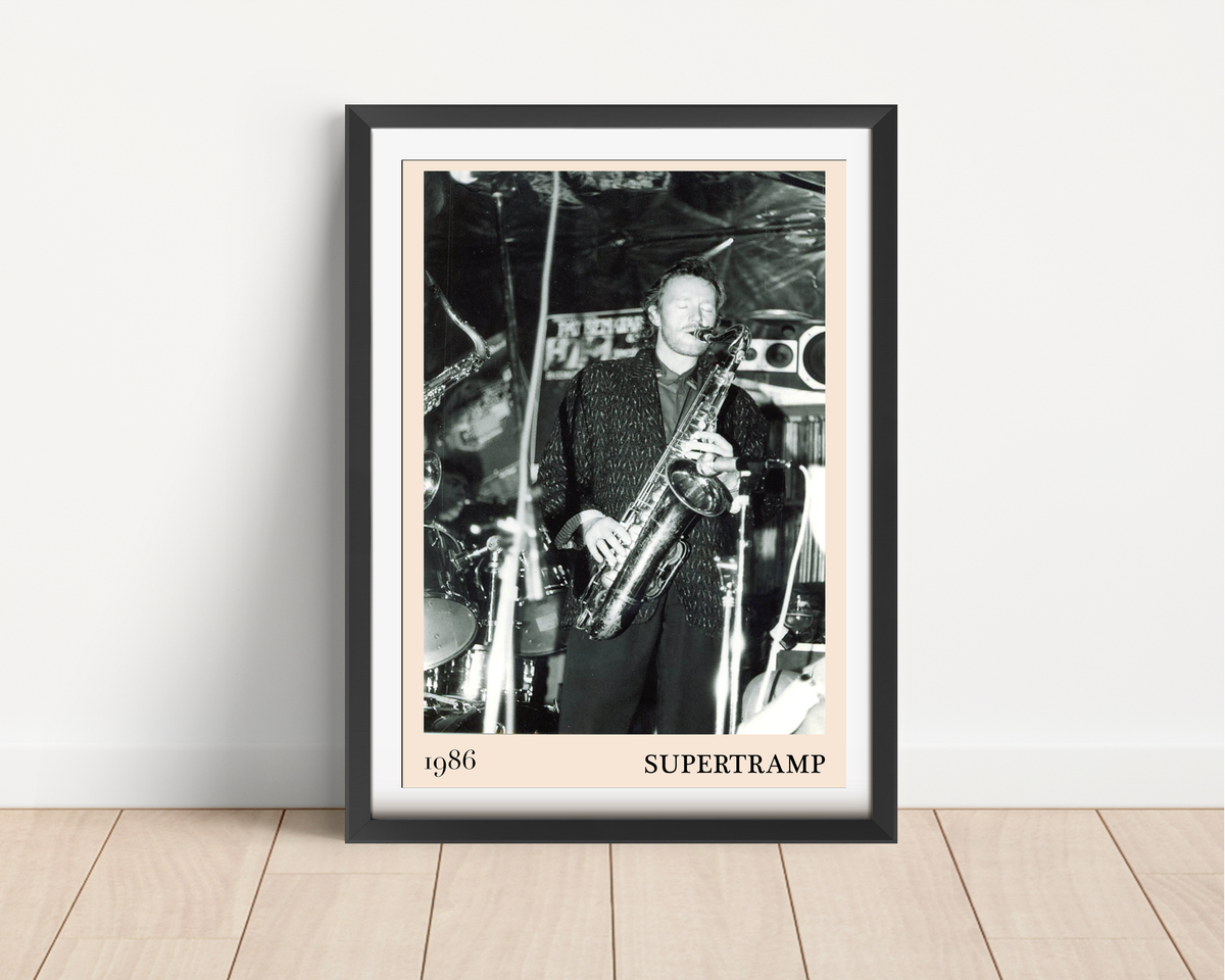 Framed Supertramp 1986 concert print leaning against a white wall on light wood flooring, featuring a black and white photo