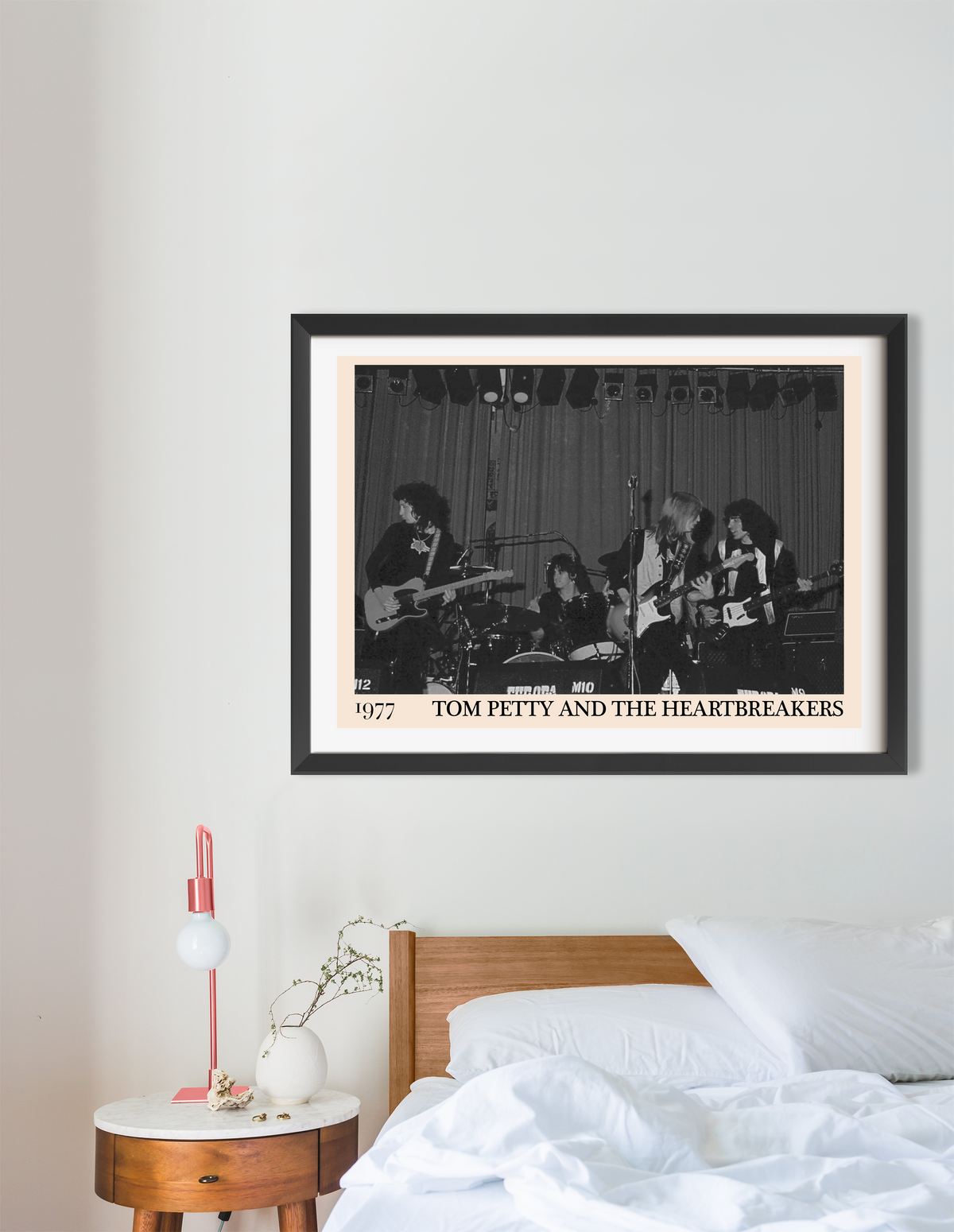 Framed print of Tom Petty and the Heartbreakers 1977 concert in black and white, hung above a wooden bed in a minimal