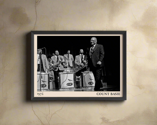 1974 photo of Count Basie crafted into a black framed-poster, hanging on a light brown rustic concrete wall in dappled sunlight