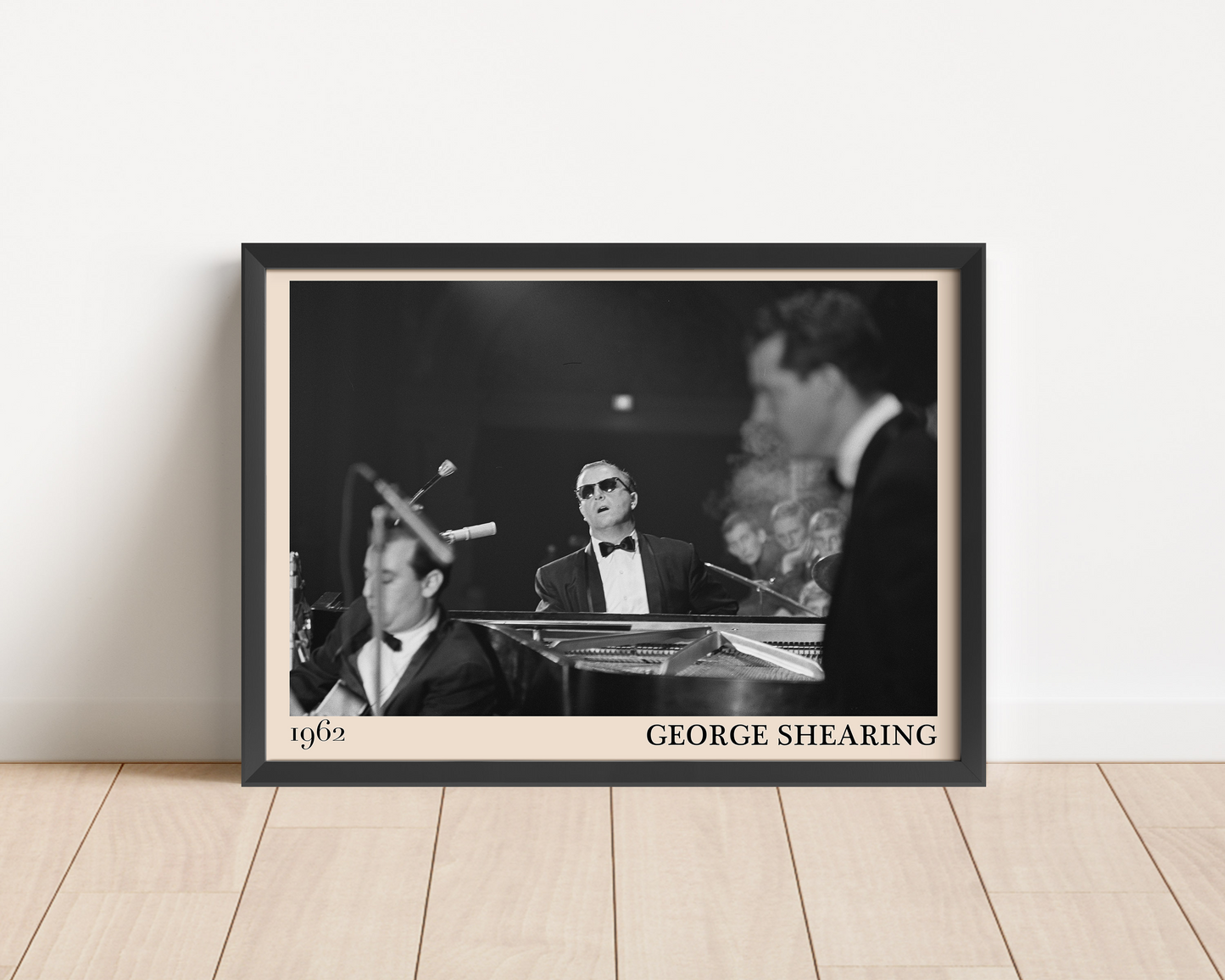 1962 picture of George Shearing playing piano. Picture crafted into a black framed poster, with an off-white border. Poster is propped against a white wall