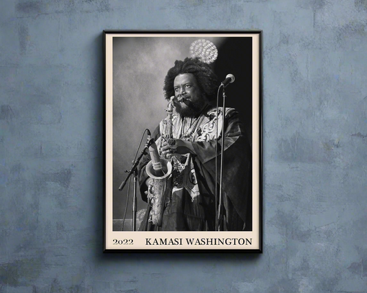 2022 photo of Kamasi Washington crafted into a black framed-poster, hanging on a blue rustic concrete wall in dappled sunlight