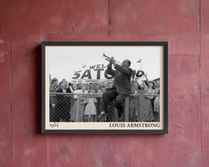 1954 print of Louis Armstrong playing trumpet on a fence. Picture crafted into a black framed poster, with an off-white border. Poster is hanging on a rustic red wall