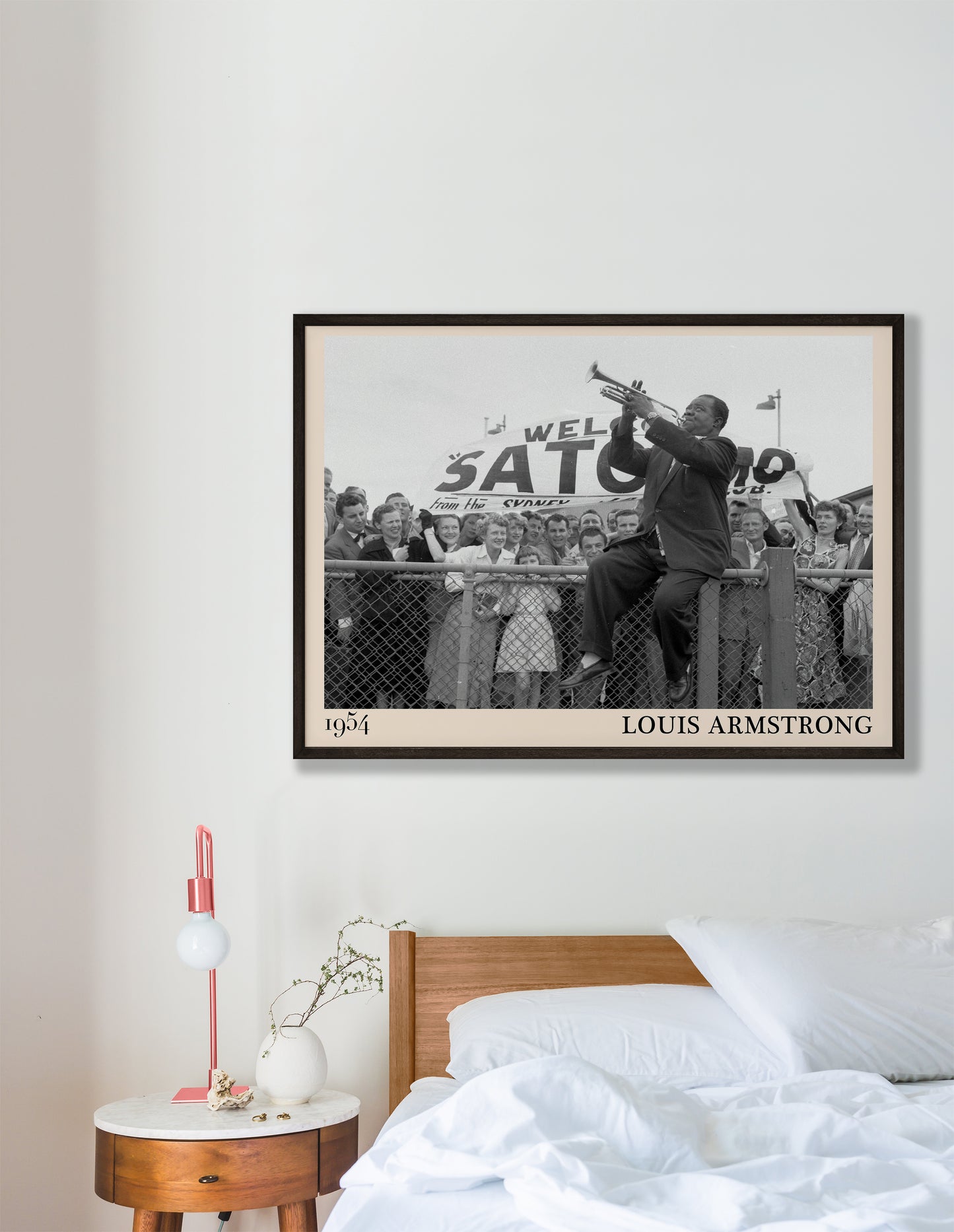 1954 picture of Louis Armstrong playing his trumpet sat on a fence. Picture crafted into a cool black framed jazz print, with an off-white border. Poster is hanging on a grey bedroom wall