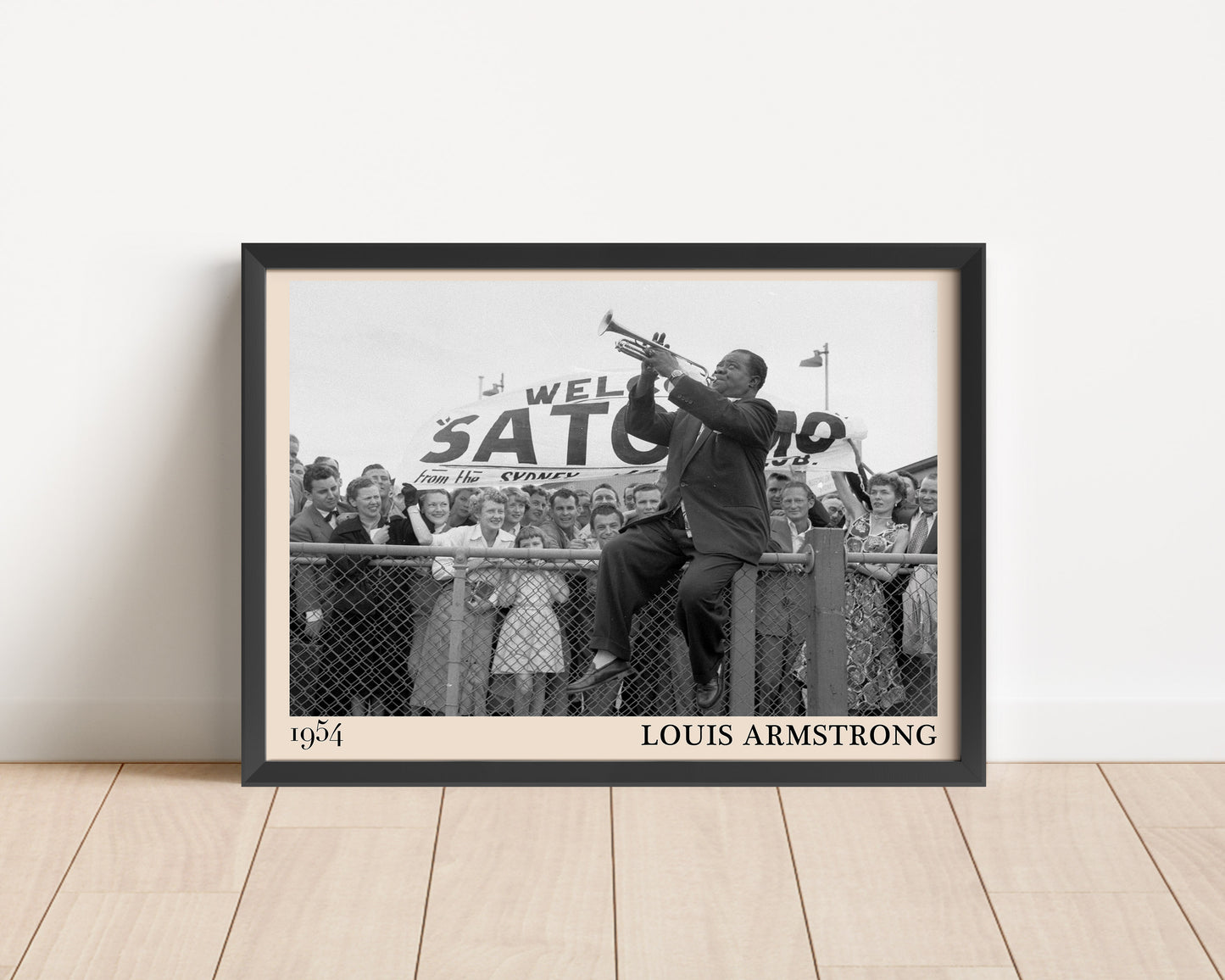 1954 print of Louis Armstrong playing trumpet on a fence. Picture crafted into a black framed poster, with an off-white border. Poster is propped against a white wall