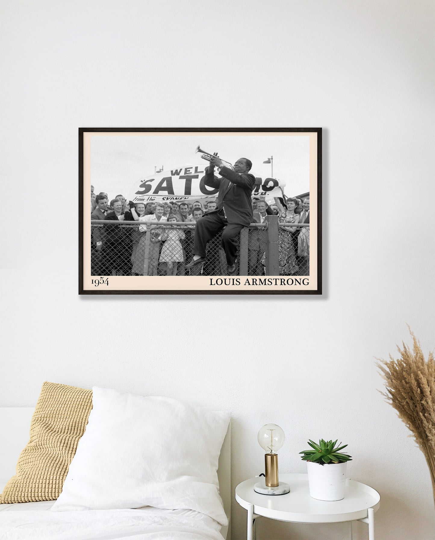 1954 picture of Louis Armstrong playing his trumpet sat on a fence. Picture crafted into a cool black framed music poster, with an off-white border. Poster is hanging on a white bedroom wall