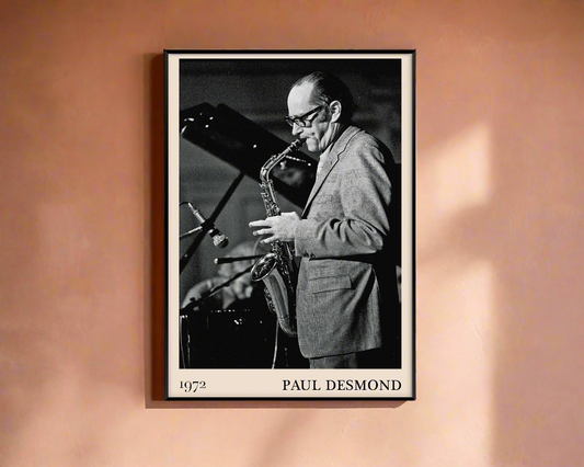 1972 photo of Paul Desmond crafted into a black framed-poster, hanging on a peach coloured concrete wall in dappled sunlight