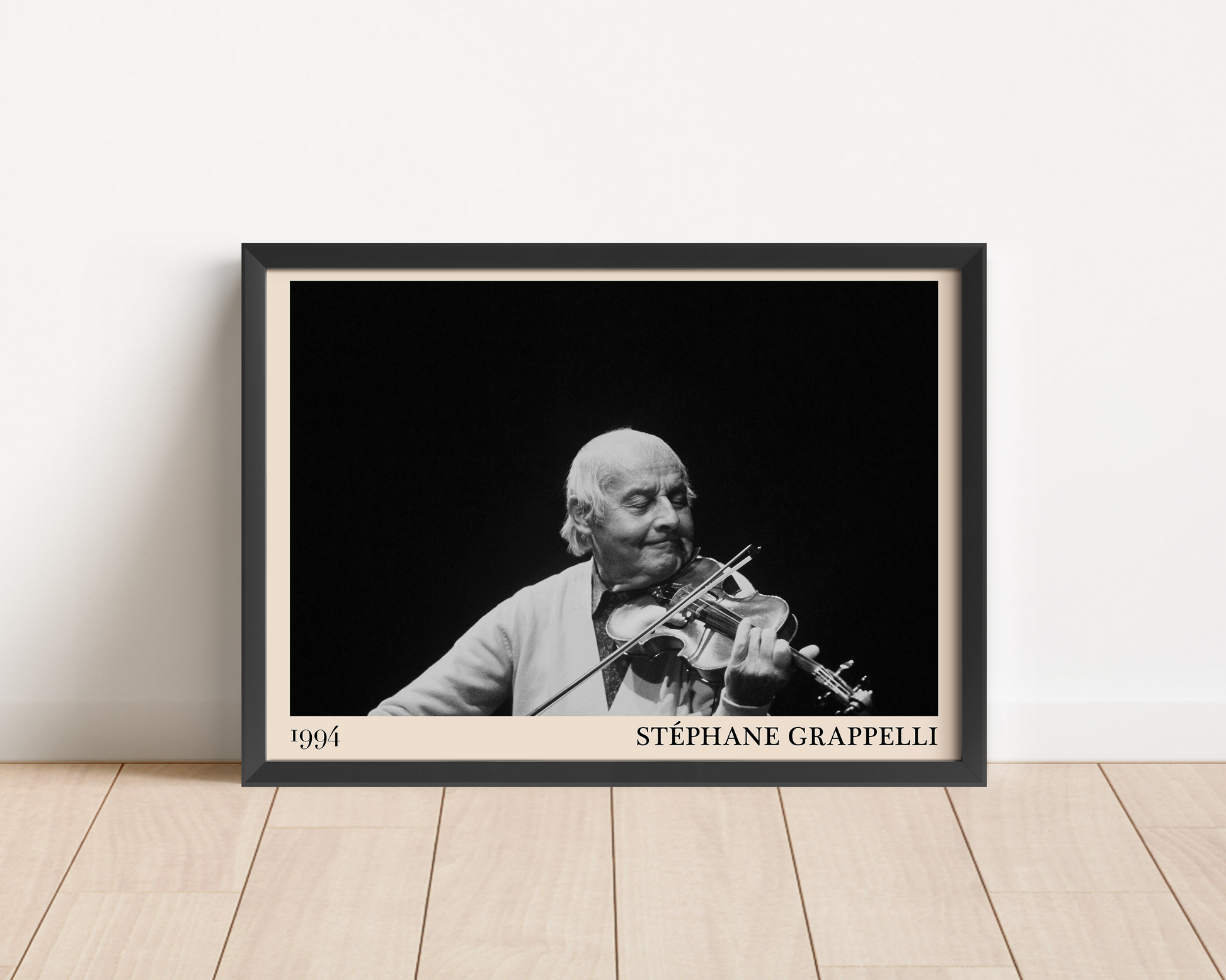 Black framed poster of Stephan Grappelli leaning against a white wall.