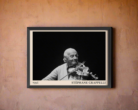 Black framed poster of Stephan Grappelli leaning against a peach coloured concrete wall in dappled sunlight