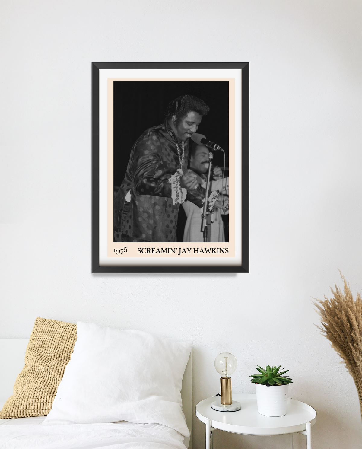 Framed Screamin' Jay Hawkins 1975 concert print in a black frame, hung above a bed with a white pillow and bedside table.