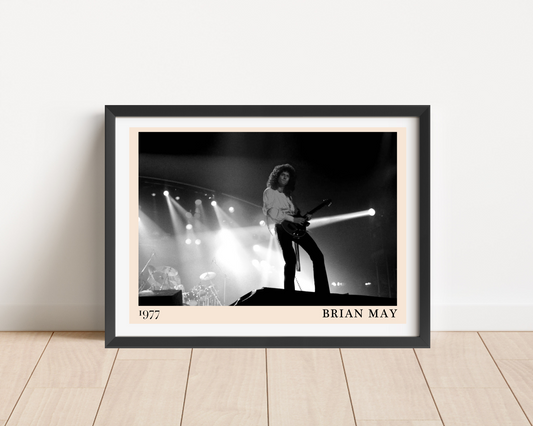 Black framed print of Brian May on stage in 1977, shown in a black and white concert photo, leaning against a white wall on