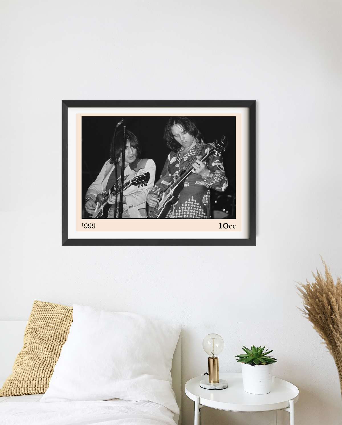 Framed 10cc rock concert print in black and white, mounted with a cream border, hanging above a bedside table in a minimal