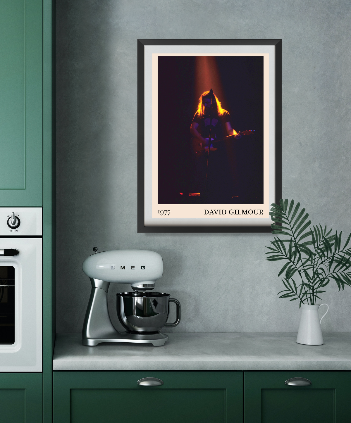 David Gilmour 1977 framed print hanging on a grey kitchen wall above a Smeg stand mixer and white vase with palm leaves.