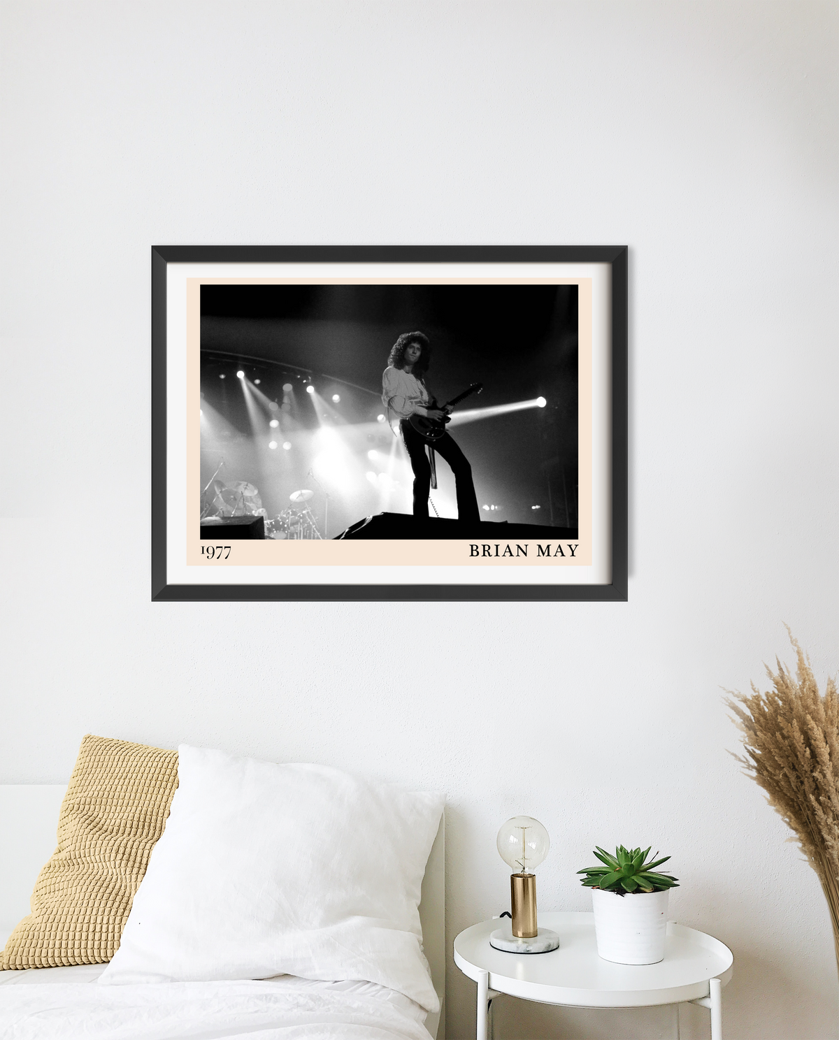 Framed print of Brian May on stage in 1977, in black and white with a cream mount and black frame, hung above a bedside