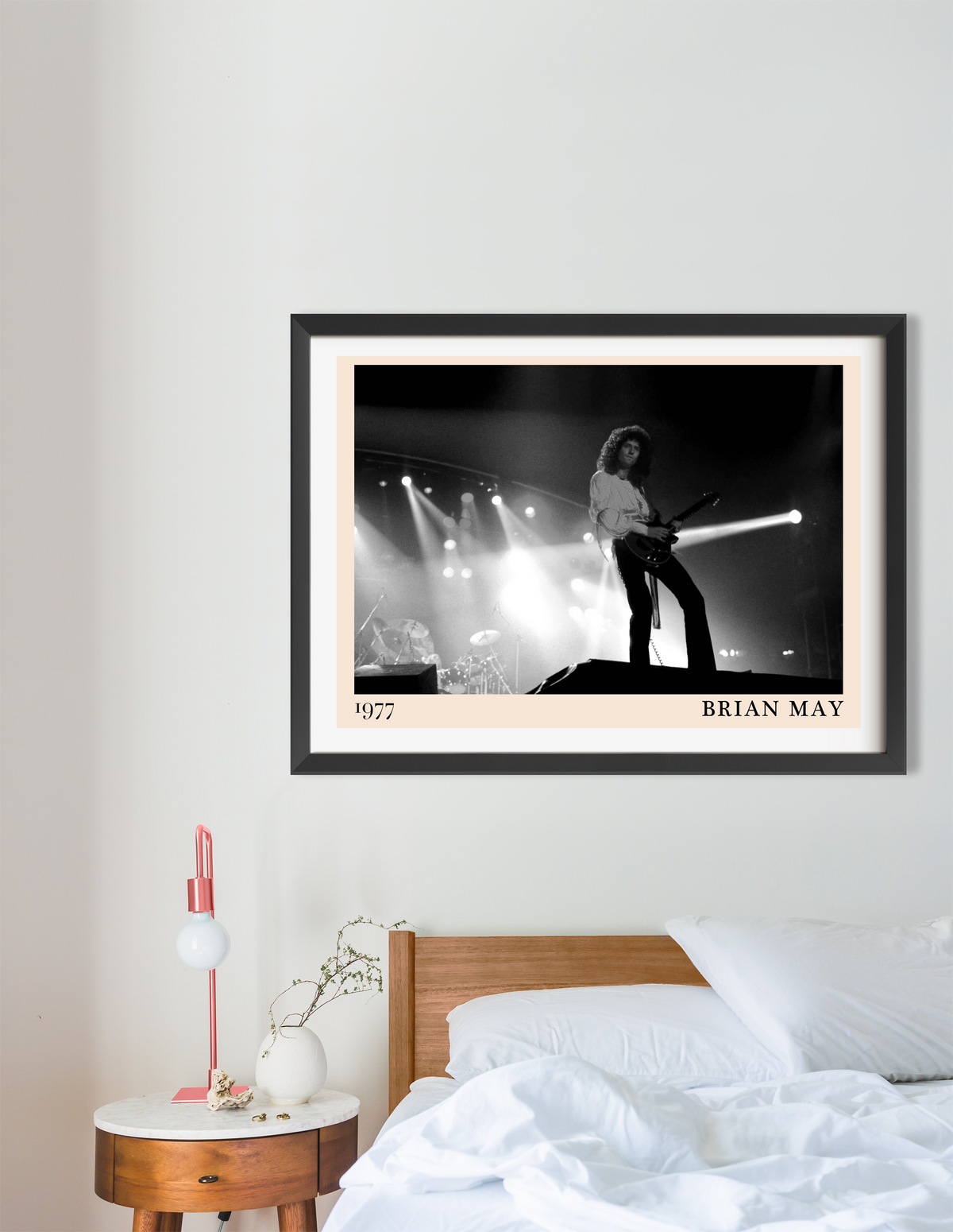 Framed print of Brian May on stage in 1977, in black and white with a peach mount, hung above a wooden bed in a minimal