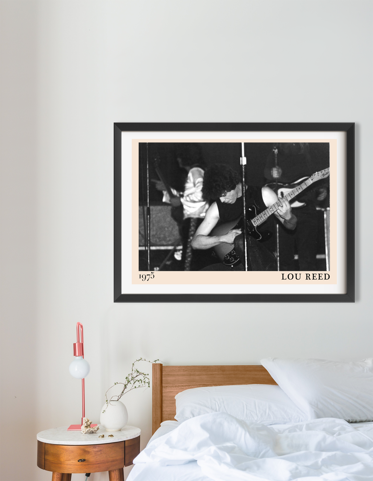 Lou Reed 1975 framed print in black frame, black and white concert photo, displayed above a wooden bed in a minimal bedroom.
