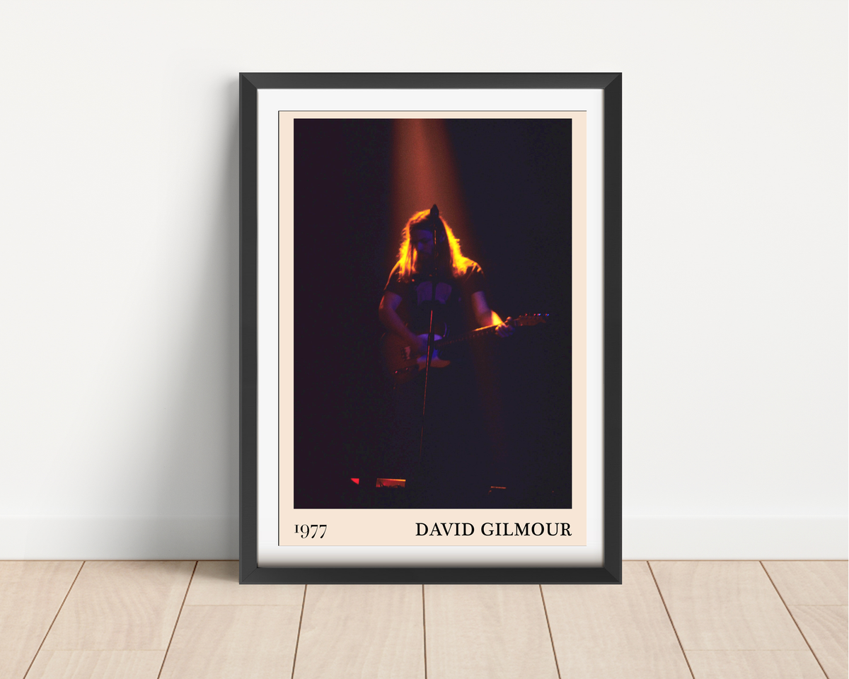 David Gilmour 1977 framed print leaning against a white wall on a light wood floor, showing a dramatic concert stage photo
