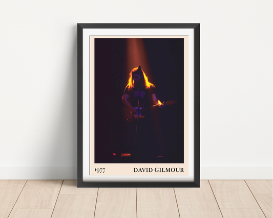 David Gilmour 1977 framed print leaning against a white wall on a light wood floor, showing a dramatic concert stage photo