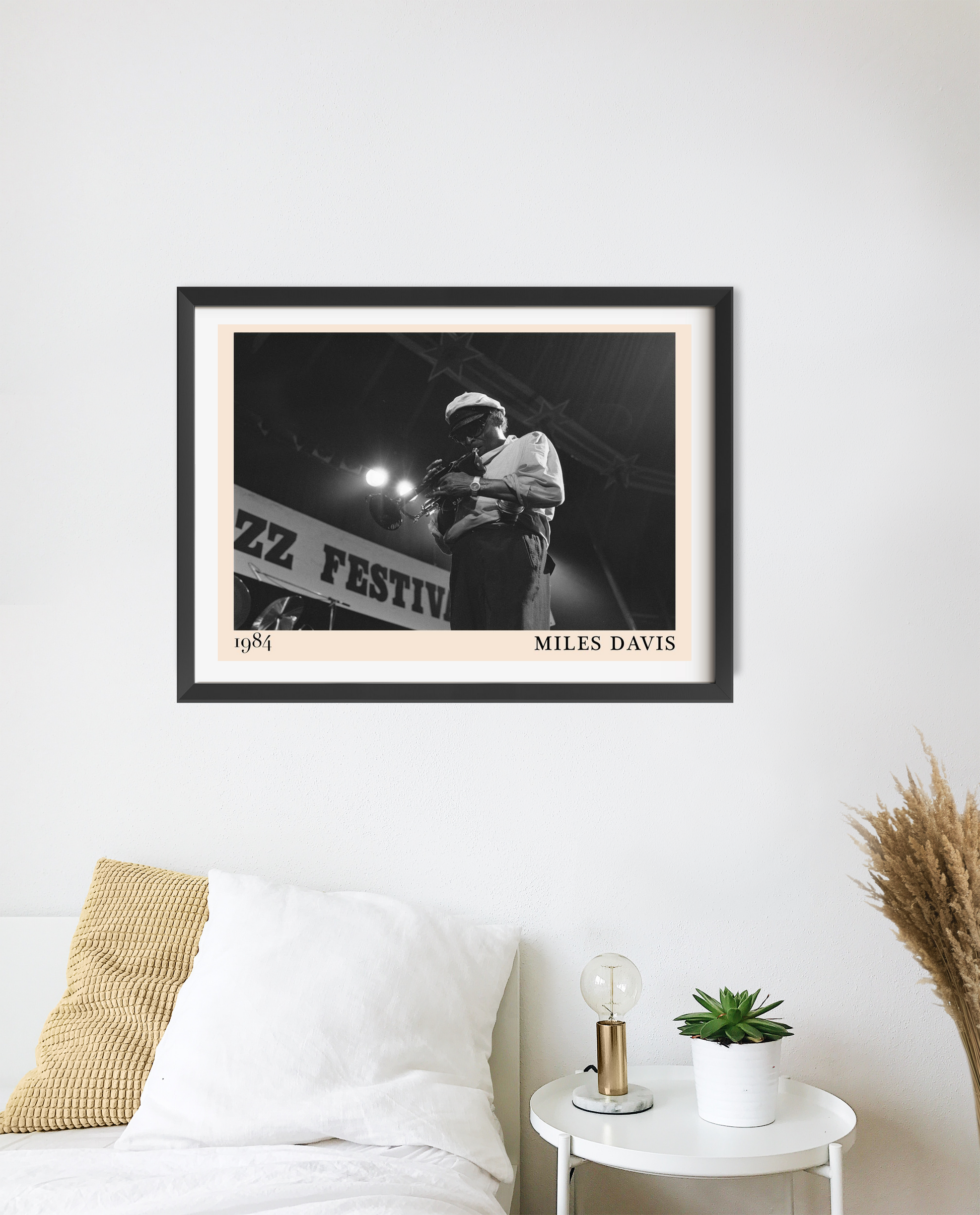 Miles Davis vintage jazz poster in a black frame on a white wall above a modern bed, featuring a monochrome festival scene.